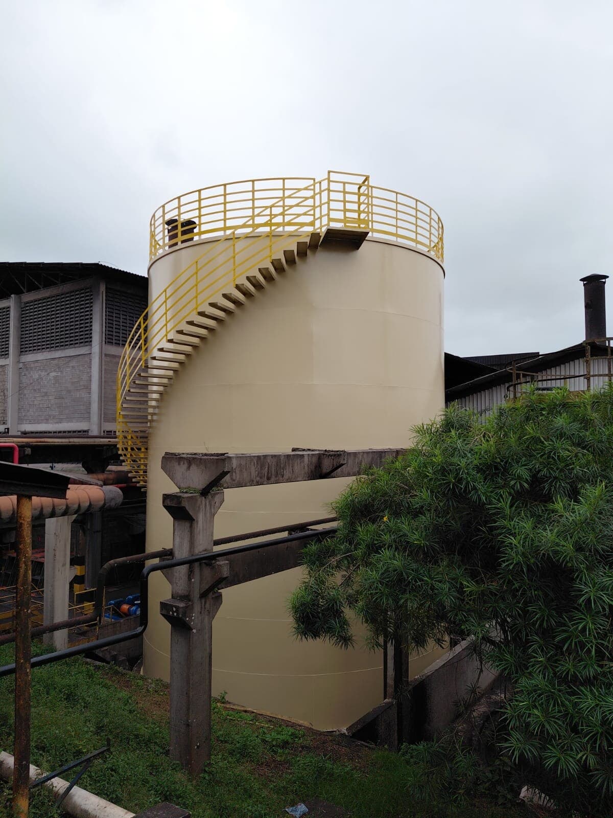 Reservatório metálico vertical com escada caracol instalado em planta industrial